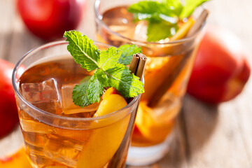 Refreshing peach iced tea in glass with ice cubes and cinnamon on wooden table