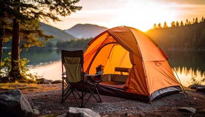 Sunrise illuminates an orange tent pitched lakeside, a folding chair sits nearby