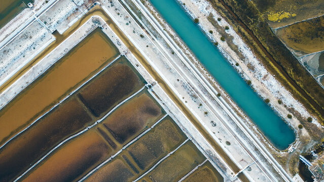 Aerial view of geometric salt pans reflecting the sky, creating a mosaic of earthy browns and striking blues, Pag, Zadar County, Croatia.