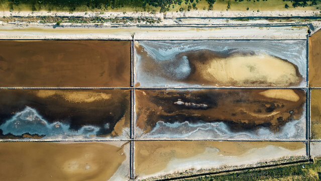 Aerial view of geometric salt pans reflecting the sky, creating a mosaic of earth tones and azure hues in a striking display of natural artistry, Pag, Zadar County, Croatia.
