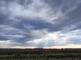 Obraz premium Stormy sunset sky over a hill in a green field. Sun rays break through the clouds