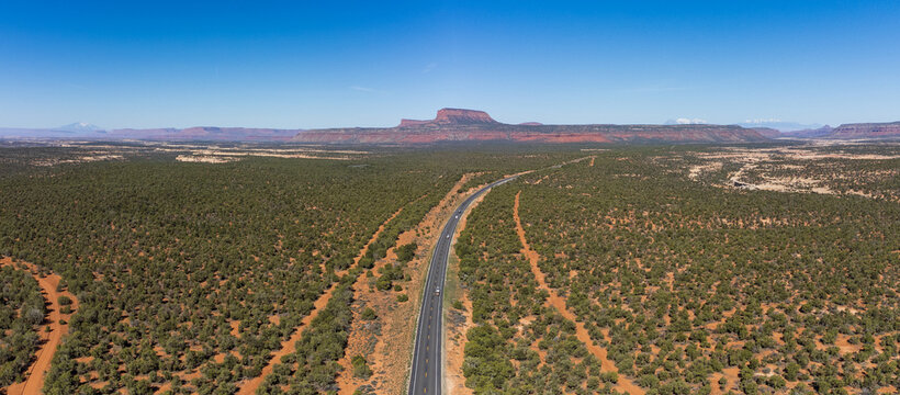 Aerial view of Utah State route 95 cutting through the arid landscape towards mesas under a vast blue sky, Lake Powell, Utah, United States.