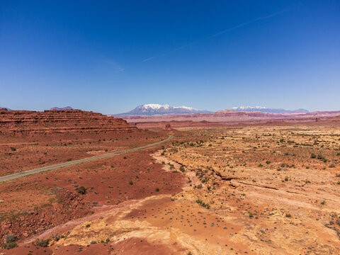 Aerial view Utah State route 95 and of a stark, terracotta landscape meets a distant, snow-capped mountain range under a clear azure sky, Lake Powell, Utah, United States.