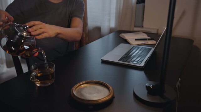 Man pouring tea at home workspace with laptop