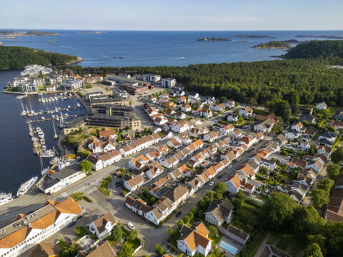 Aerial view of the vibrant coastal town nestled between the serene harbor dotted with boats and the lush green forest, Mandal, Agder, Norway.
