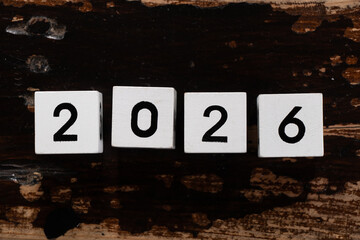 White cubes with black numbers lined up in a row symbolize the year 2026 and lie on an old wooden table
