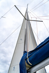 Obraz premium Low-angle view of sailboat's mast and furled blue main sail against bright, cloudy sky, showcasing intricate rigging and nautical details