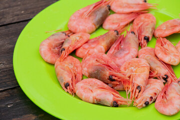Boiled pink shrimps laid out in a green plastic plate, which stands on an old wooden table