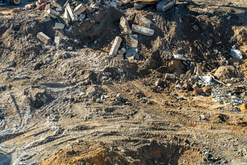 High-angle view of vast construction or demolition site showing messy mounds of earth, scattered concrete rubble, and heavy machinery tracks on rough ground.