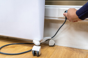 Close-up of person's hand plugging black electrical power cord from white portable appliance with...