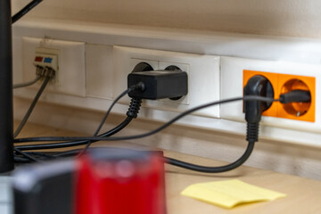 Row of power outlets and data ports with plugs and cables, including black charger and orange...