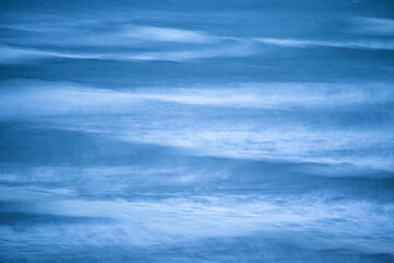 Long exposure creating an abstract impression of ocean waves with flowing streaks of soft blue and...
