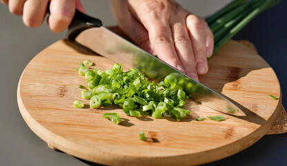 chef cuts fresh green onion on cutting board