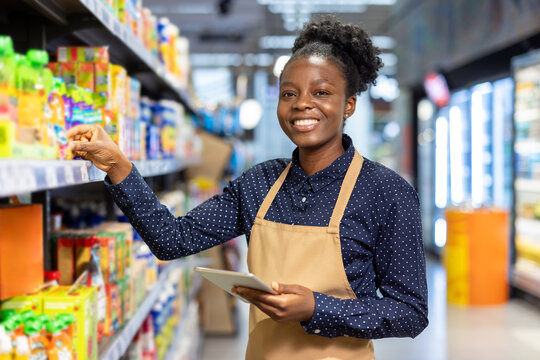 Smiling employee organizing shelves with a tablet in a grocery store - Powered by Adobe