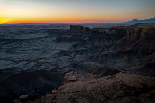 Aerial drone view of Moonscape Overlook, USA, at sunrise. A lone woman stands small against the vast, rugged lunar-like landscape, enjoying the serene and dramatic natural beauty.