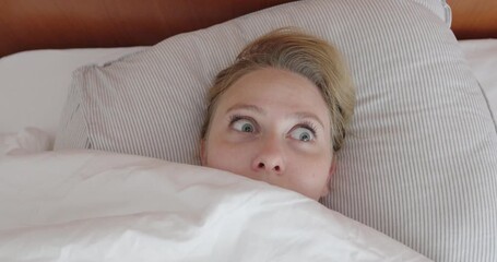 Close-up of a woman lying in bed, suddenly opening her eyes wide in shock. Her startled facial expression reflects fear, surprise or a bad dream. - Powered by Adobe