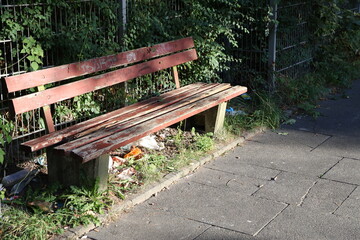Old wooden bench in urban park with litter and greenery