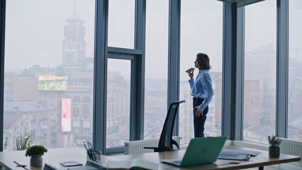 Business manager recording voicemail at smartphone standing by office window.