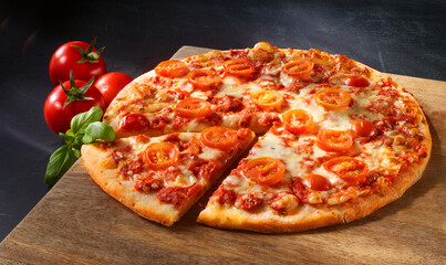 Pizza mit Tomaten und Kaese ueberbacken mit Basilikumzweig und rohe Tomaten auf rustikaler Holzplatte, Italien, Pizzastück, 