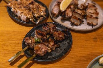 Grilled chicken and scallion yakitori skewers glazed in sauce, served on a rustic dark plate among other Japanese grilled dishes