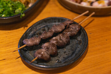 Another angle of grilled chicken heart yakitori skewers on a rustic plate, close-up showcasing texture and juicy glazed surface
