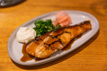 Grilled teriyaki salmon fillet with glistening glaze served with pickled ginger, scallions, and a dollop of creamy mayonnaise on white plate
