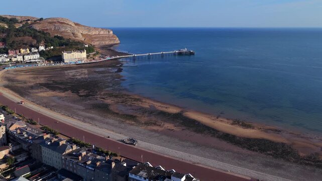 Aerial video of Llandudno Pier stretching into the sea beside the cliffs of the Great Orme on a summer day. 