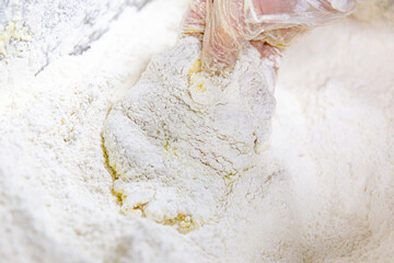 Raw chicken being pressed into flour for breading, gloved hand coating fillet evenly, close-up food preparation in kitchen setting