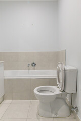 White ceramic toilet and built-in bathtub with tiled walls and floors, clean minimalist bathroom layout with neutral color palette