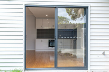 Sliding glass door entry to kitchen space with white cabinets, wooden floor and grey backsplash, modern minimalist interior design