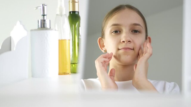 Young Girl Applying Lotion in Mirror, Teenager Use Moisturizer for Dry Skin in Bathroom, Child use Face Cream, Blonde Kid