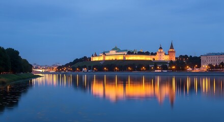 Obraz premium A tranquil evening view of a historic castle complex reflected serenely in the calm waters of a river, showcasing the illuminated structures and surrounding greenery.
