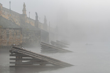 A fisherman boat in the mist by the the Charles Bridge in the UNESCO city site Prague in Czech republic.