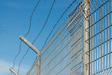 Closeup of a metal chain link fence with a clear blue sky background.	