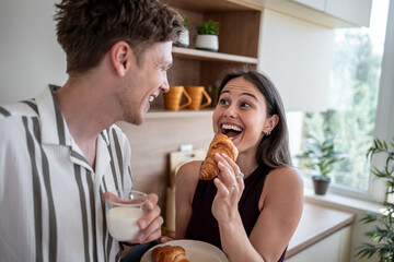 Happy couple enjoying breakfast with croissants and milk in kitchen