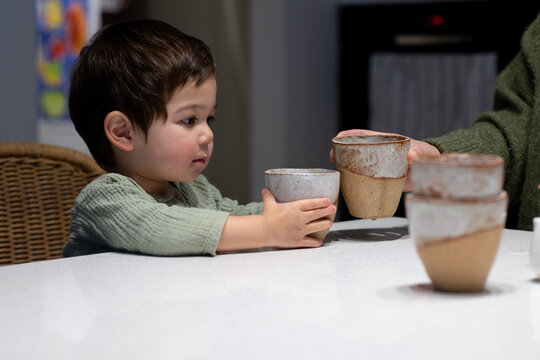 Child and Adult clinking Cups with Teapot on Kitchen Counter