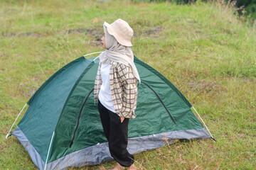 Sporty Muslim Asian woman standing near tent and backpack, enjoying sunny afternoon in the mountains. Camping lifestyle concept