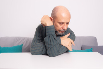 Serious, bald man in a formal shirt with a beard, sitting with his arms resting on a table,...