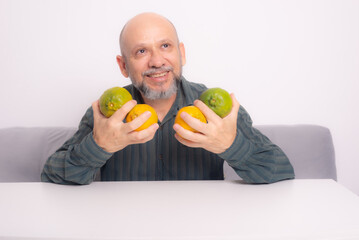 Smiling bald man with a beard in a green dress shirt holding four tangerines in his hands.