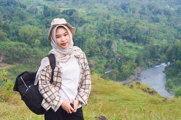 Sporty Muslim Asian woman standing near tent and backpack, enjoying sunny afternoon in the mountains. Camping lifestyle concept