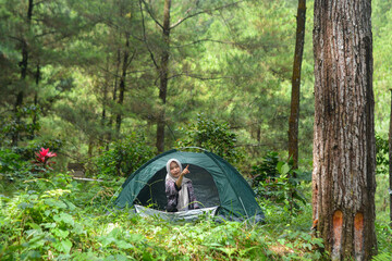 Sporty Muslim Asian woman standing near tent and backpack, enjoying sunny afternoon in the mountains. Camping lifestyle concept