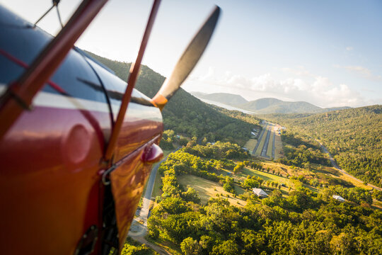 View from biplane approaching airstrip through tropical mountain valley in late afternoon light.