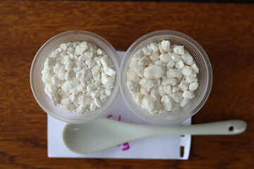Large hygroscopic granules of calcium chloride in two plastic cups. Used as an additive for concrete to increase strength.