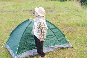 Sporty Muslim Asian woman standing near tent and backpack, enjoying sunny afternoon in the mountains. Camping lifestyle concept