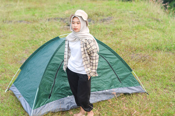 Sporty Muslim Asian woman standing near tent and backpack, enjoying sunny afternoon in the mountains. Camping lifestyle concept