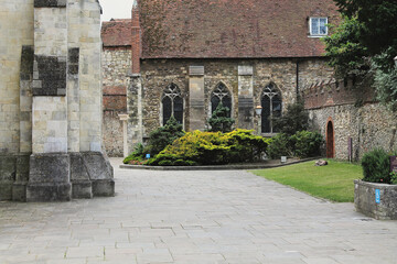 Medieval cathedral courtyard featuring Gothic stone architecture, arched windows, mixed stone and brick construction with landscaped garden area