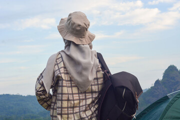 Sporty Muslim Asian woman standing near tent and backpack, enjoying sunny afternoon in the mountains. Camping lifestyle concept