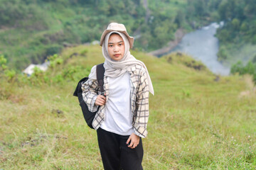 Sporty Muslim Asian woman standing near tent and backpack, enjoying sunny afternoon in the mountains. Camping lifestyle concept