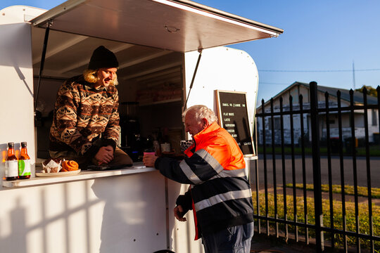 happy older Aussie workman in high vis workwear buying warm takeaway coffee from van
