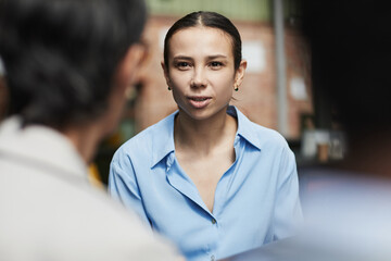Portrait of young Caucasian woman engaging in conversation with two work colleagues, maintaining...